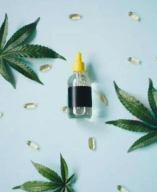 A bottle of cbd oil surrounded by cannabis leaves.
